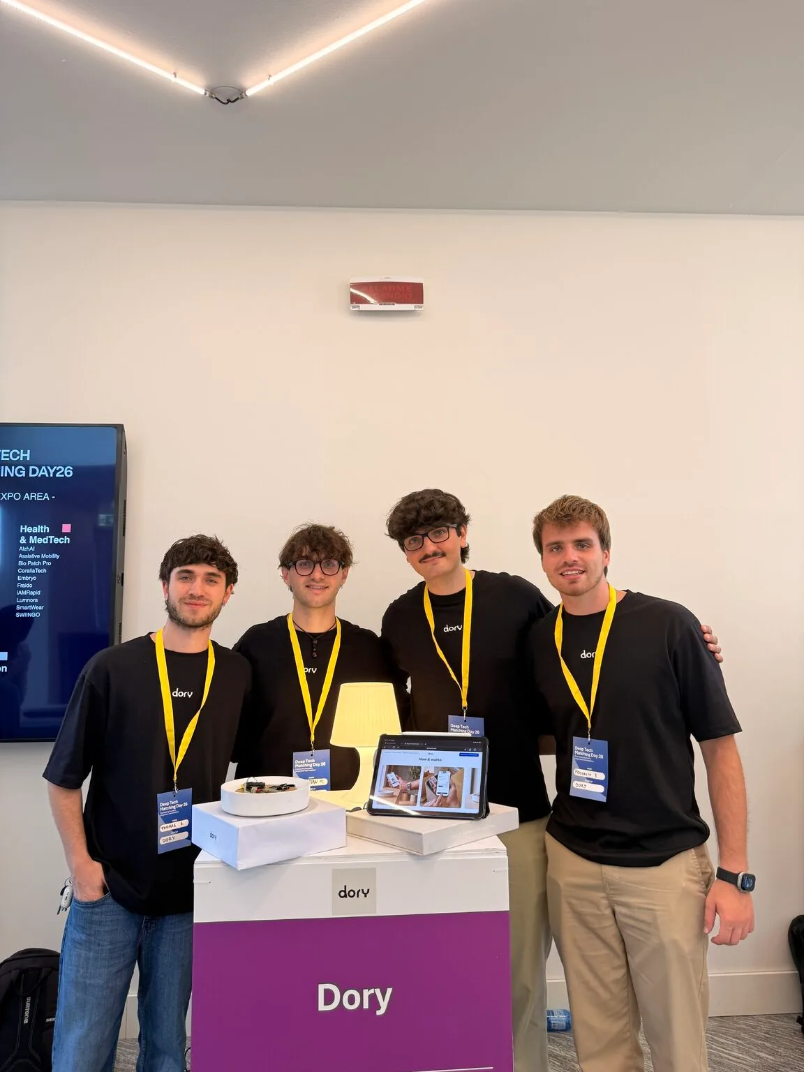 The four Dory founders behind their counter, with Dory, a lit lamp and a tablet running the demo.